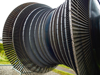 Massive industrial turbine rotor with closely spaced, curved metal blades arranged in concentric rows, displayed outdoors on a gravel platform in a grassy area.