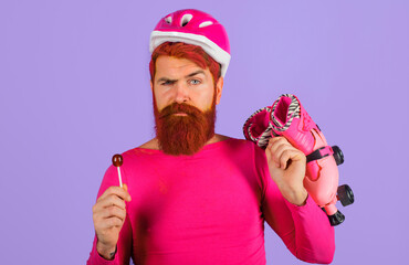 Bearded guy in pink sweater with dyed hair and beard in protective helmet holds roller skates....