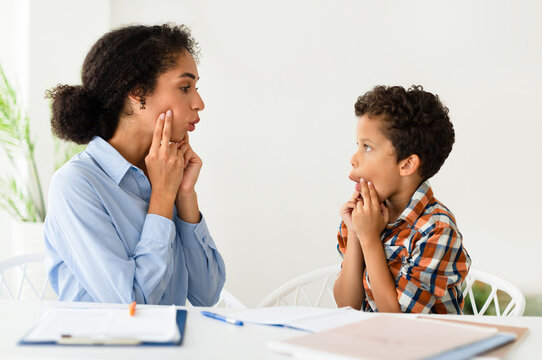 Speech Therapy Session. Woman working on kid boy pronunciation sitting at desk indoors. Professional speech therapist lady helping little patient with stuttering issue. Logopedic correction