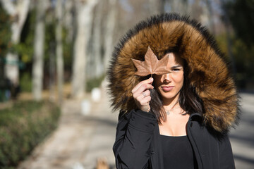 Portrait of a young, beautiful, dark-haired woman in a fur hooded coat, covering her eye with a dry...