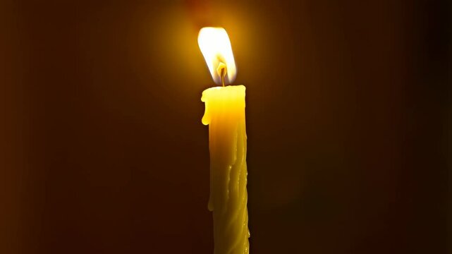 Single burning candle with glowing flame against a dark background casts a warm and inviting glow.