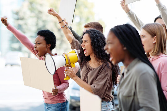 Active young people making strike on the street, using loudspeaker, holding blank placards, side view, copy space. International group of angree demonstrators fighting against war