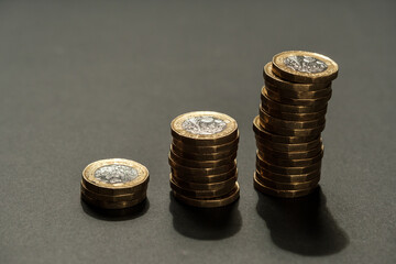 Three ascending stacks of British one pound coins arranged on a dark surface, symbolising financial growth, savings, and economic progression, Stafford, United Kingdom, May 18, 2025..
