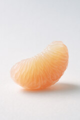 Single grapefruit segment with soft translucent glow on white surface