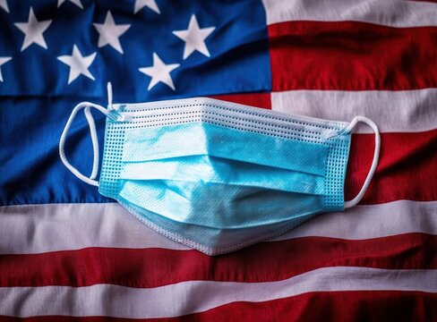 Blue surgical mask placed on a United States flag symbolizing health protection and pandemic impact