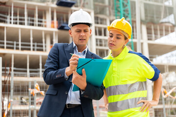 Civil engineer and a young woman worker working on a construction site discuss a construction plan,...