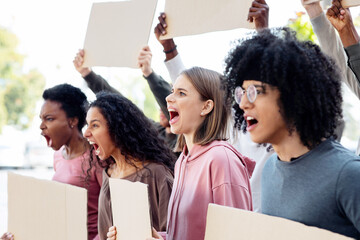 Motivated group of international students with blank placards making protest outdoors, chanting...