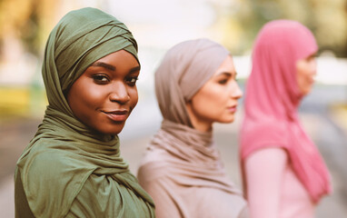 Black Muslim Woman Looking At Camera Posing With Diverse Islamic Ladies Standing In Line Outdoor In City Park, Wearing Hijab Headscarf. Diversity And Equality Concept. Selective Focus.