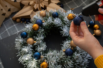 Crafter using hot glue DIY process of woman making Christmas arrangement with decor of blue and...