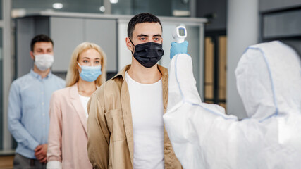 New normal and coronavirus disease control. Medic in protective uniform with infrared thermometer...