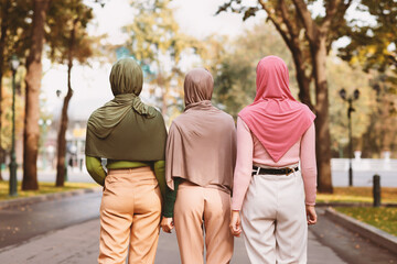 Back View Of Three Modern Muslim Women Walking Together Wearing Hijab Headscarves In City Park...
