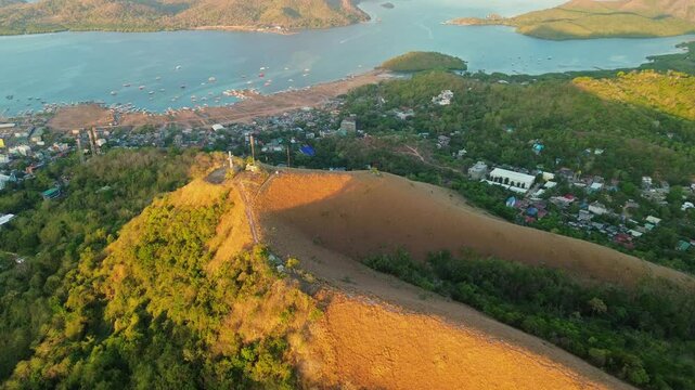 Golden sunrise aerial view over Mount Tapyas hillside toward Coron town harbor boats dry grass and island bay water in Palawan