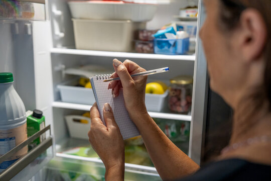 Organized woman plans her grocery shopping while checking the fridge contents