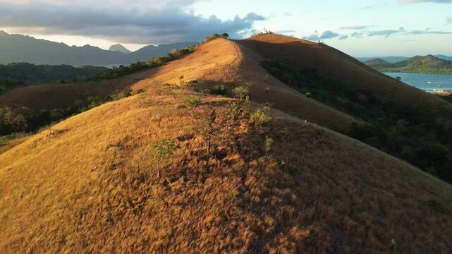 Golden sunrise light across dry Mount Tapyas grass hills in Coron with narrow ridge trail warm shadows and bay water glimpse in Palawan