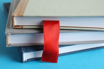 Book with red ribbon bookmark and colorful ones on light blue background, closeup