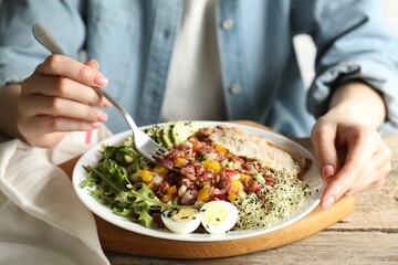 Woman eating delicious salad with brown rice at wooden table, closeup