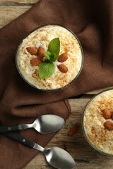 Delicious rice pudding with cinnamon, almonds and mint served on wooden table, flat lay