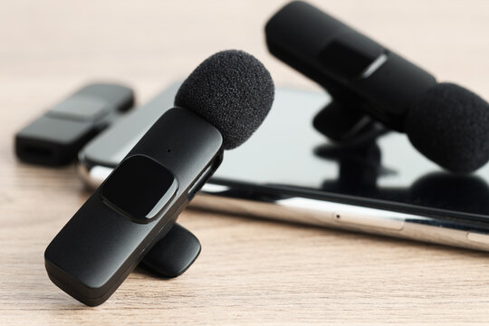 Lavalier microphones and smartphone with wireless receiver on wooden table, closeup