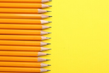 Sharp graphite pencils on yellow background, flat lay. Space for text