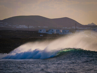 Lines of waves roll toward the volcanic shore of Lanzarote, big offshore mist swirling above their...