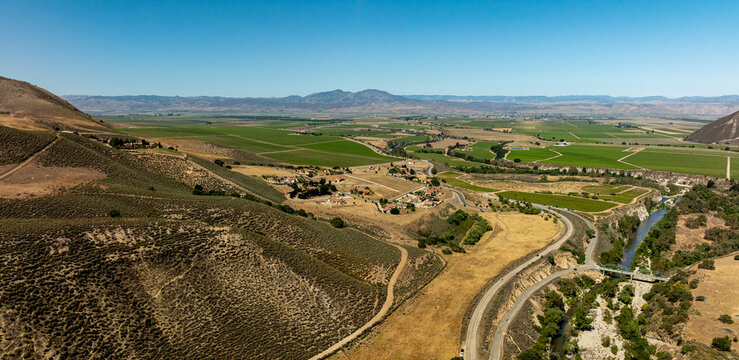 Afternoon sunlight touches spring vineyards in a panoramic landscape of rolling hills and distant mountains under a vast sky.  Aerial view of Greenfield from Arroyo Seco