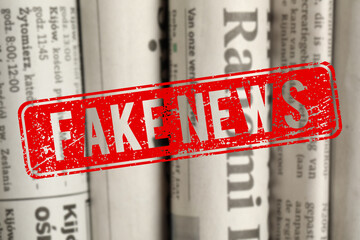 Red Fake News stamp and newspapers in different languages as background, closeup