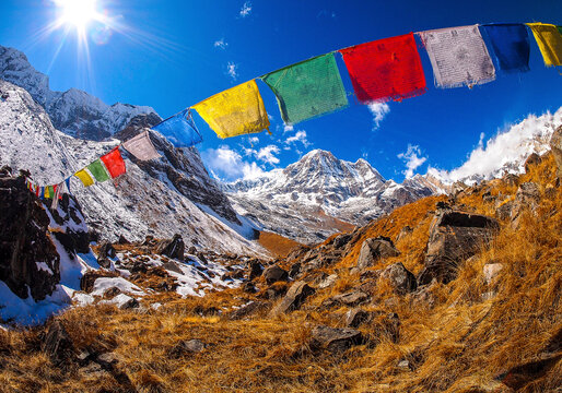 Prayer flags fluttering in high-altitude Himalayan valley with snow peaks and blue sky in background. Annapurna Himal region of north central Nepal