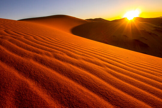 Vibrant sunset over rippled sand dunes in desert landscape with warm sunlight and dramatic shadows