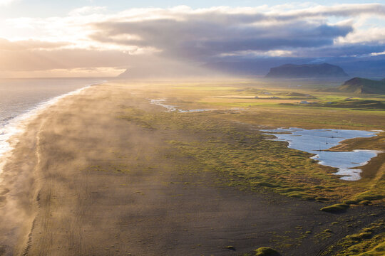 Breathtaking aerial view of Reynisfjara black sand beach with dramatic sunlight rays piercing through clouds at sunset, Vik, Iceland