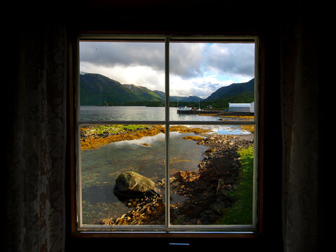 Scenic view of a peaceful Norwegian fjord and rugged mountains seen through a rustic wooden window frame, Scandinavia