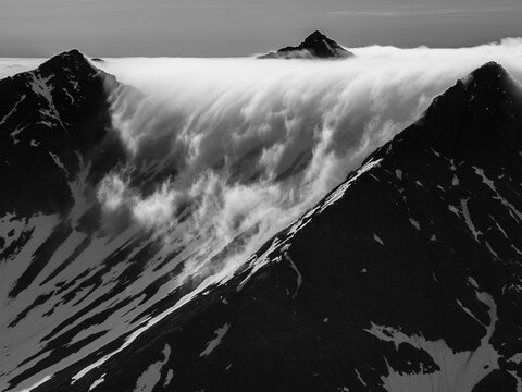 Dramatic black and white landscape of a cloud waterfall cascading over mountain peaks near Hornsund, Svalbard