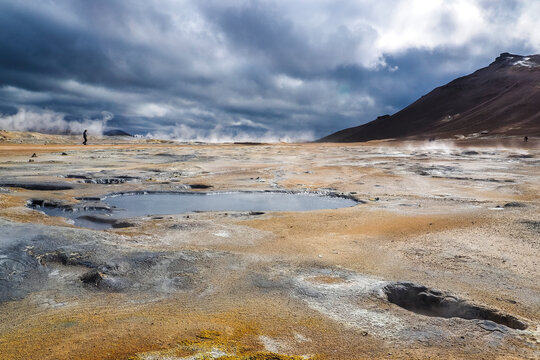 lonely person walking on Mudpots in the geothermal area Hverir, Iceland. The area around the boiling mud is multicolored and cracked.