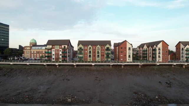 Group of similar apartment buildings on waterfront. Slide and pan shot of muddy riverbed at low tide. Newport, Wales, UK