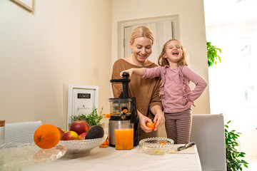 Family mother and charming little daughter preparing raw fruit juice in the cold pressed juicer in...