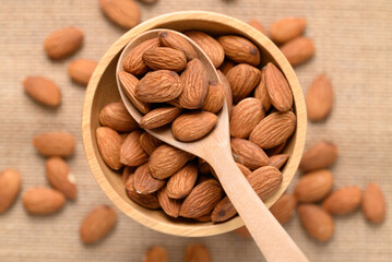 Raw almond nut seed in wooden bowl with spoon, Top view