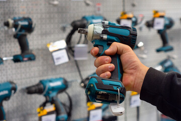 A hand holds a teal power drill in front of a hardware store display with various tools. Concept...