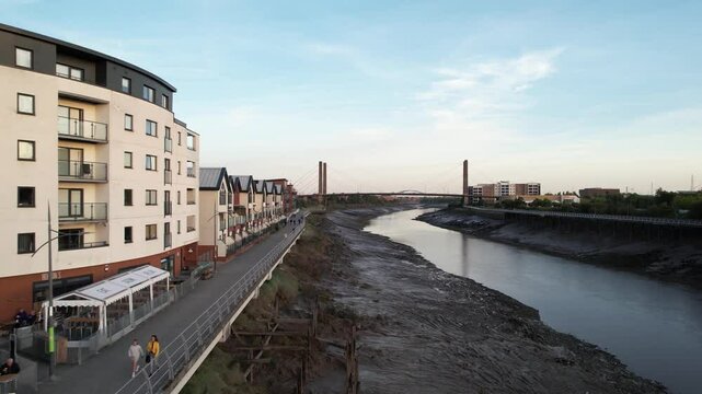  Row of apartment houses on waterfront. Backwards revealing of low water in riverbed and footbridge over. Newport, Wales, UK