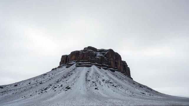 Snow covered rocky hill in middle of desert on cloudy day