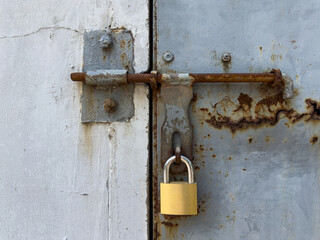 Close up of rusty vintage iron crossbar lock on grungy iron door locked with a new brass padlock.
