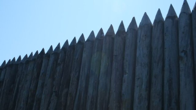 Wooden palisade made of logs. Log wooden fence. Long sharp stakes