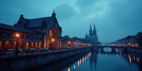 Fototapeta premium Twilight cityscape showcasing a grand arched building alongside a tranquil canal, culminating in a majestic gothic cathedral in the distance.