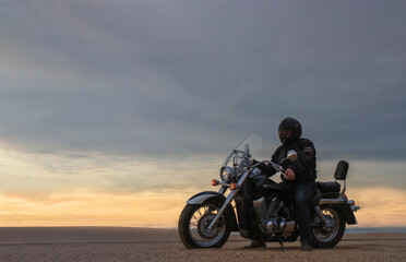 Man on motorcycle in desert during sunset with dramatic clouds &mdash; concept of freedom, travel, solitude, adventure, and outdoor lifestyle in wild open landscapes