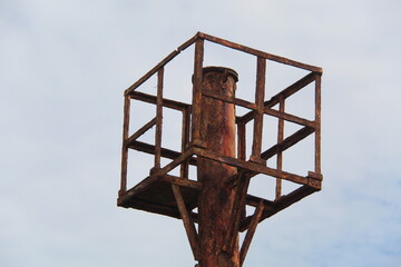 Rusty metal tower structure with a square frame against a cloudy sky background. Minimalist...