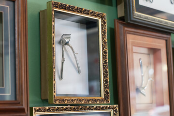 Vintage manual hair clippers and blades displayed in a shadow box frame with ornate gold detailing, mounted on a green wall.