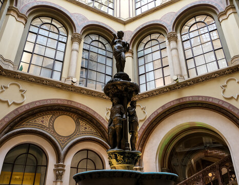 Vienna – View of the Ferstel Passage fountain, the elegant Renaissance Revival bronze sculpture surrounded by the arcade's ornate ironwork and glass-domed ceiling, creating a jewel-like centerpiece. - Powered by Adobe