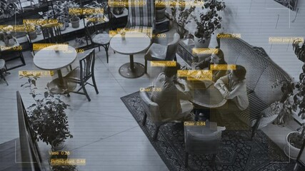 Wide top view CCTV shot of overhead surveillance camera recording and detecting customers and objects on cafe premises. Group of young friends sitting at table with laptop, enjoying fun conversation