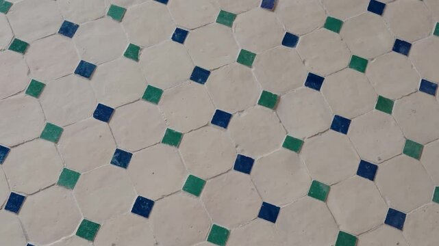 Close-up view of a Moroccan tile floor. The tiles are white with alternating small green and dark blue squares arranged in an octagonal and diamond pattern. This traditional design