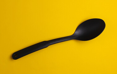 Black plastic kitchen spoon on yellow background