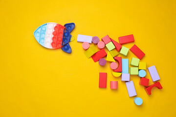 Pop it rocket and Multicolored wooden children's cubes toy different shapes on yellow background