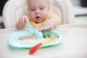 Cute little baby eats food from a plate at a table